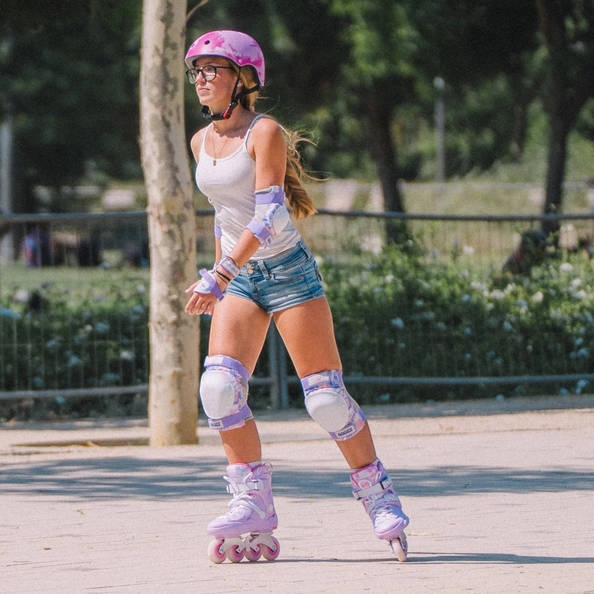 Patinadora KonRoller usando capacete FlyingEagle Urban rosa nuvem marmorizado, joelheiras e patins inline em parque